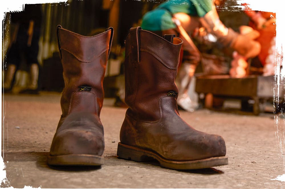 A man wearing the Serious Plus 10" Waterproof Nano Comp Toe Met Guard Puncture Resisting in Brair Oiled (brown) in a warehouse.