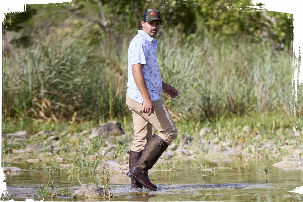 A man wearing the Brome 17" Waterproof Snake Boots in Briar Pitstop (brown) while walking through a stream.