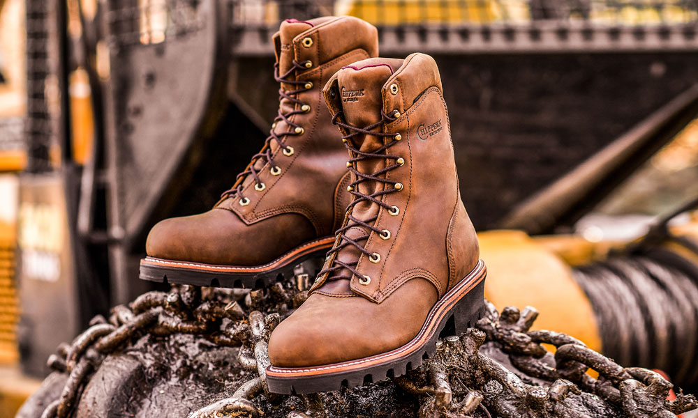 A pair of the Super Dna 9" Waterproof Steel Toe Insulated Logger in Bay Apache sitting on a tractor tire. 