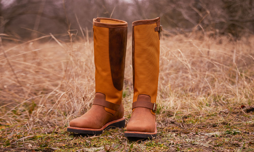 A pair of the Cottonwood 17" Snake Boot in Hickory Brown laying in a field.